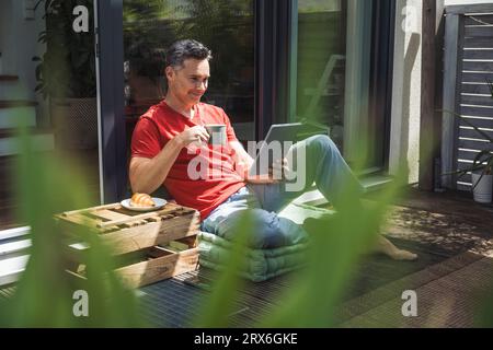 Uomo che si rilassa sul balcone con tablet digitale e tazza in mano Foto Stock