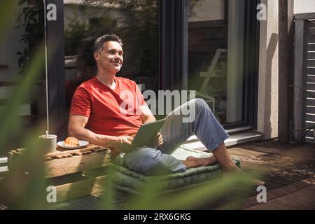 Uomo che si rilassa sul balcone con un tablet digitale nelle mani Foto Stock