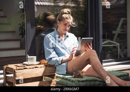 Donna che si rilassa sul balcone con un tablet digitale in mano Foto Stock