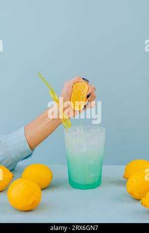 Mano di una donna che spreme il limone in un bicchiere da cocktail sul tavolo Foto Stock