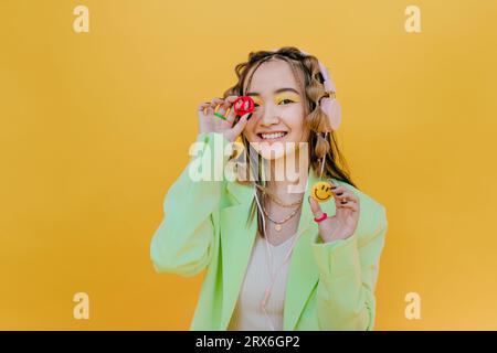 Donna sorridente con cuffie che reggono smiley su sfondo giallo Foto Stock