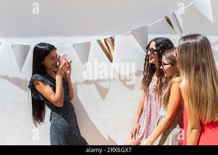 Donna sorridente che fotografa amici con la fotocamera davanti al muro Foto Stock