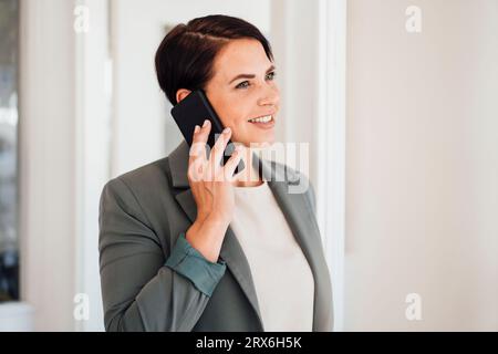 Donna d'affari sorridente che parla con lo smartphone in ufficio Foto Stock