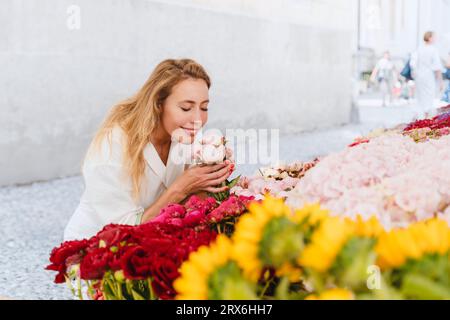 Donna sorridente che puzza di fiori al mercato Foto Stock