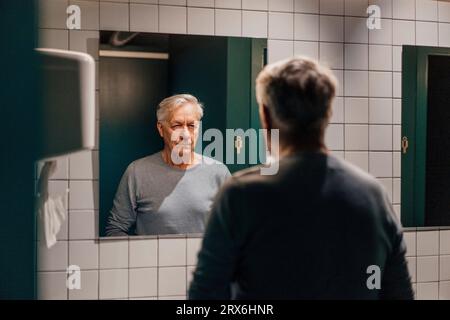 Senior uomo cercando in specchio nella sala da bagno Foto Stock