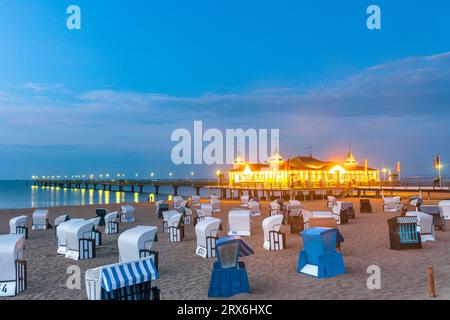 Germania, Meclemburgo-Vorpommern, Ahlbeck, sedie a sdraio con cappuccio e molo illuminato al tramonto Foto Stock