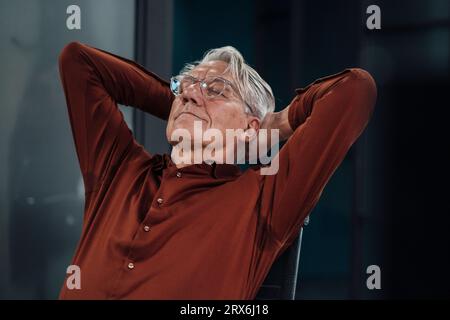 Uomo d'affari anziano con le mani dietro la testa che dorme in ufficio Foto Stock