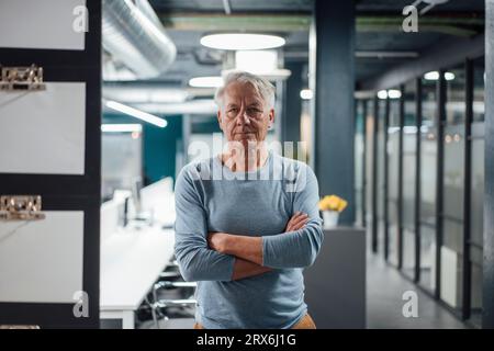Uomo d'affari sicuro di sé con le braccia incrociate in ufficio Foto Stock