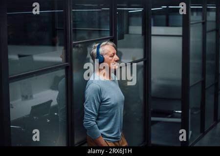 Uomo d'affari anziano che ascolta musica con le cuffie sul posto di lavoro Foto Stock