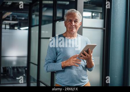 Uomo d'affari anziano sorridente che tiene un tablet PC al posto di lavoro Foto Stock