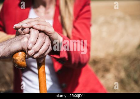Donna e uomo anziano che mettono le mani su un bastone Foto Stock