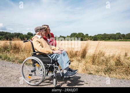 Uomo anziano seduto in sedia a rotelle da una donna e guardando il campo Foto Stock