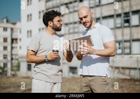 Gli architetti collaborano a un progetto architettonico, discutendo progetti e progetti per un edificio moderno. Lavorare insieme all'aperto, dimostrazioni Foto Stock