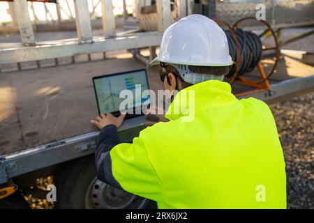 Ingegnere che lavora su un computer portatile vicino a una macchina per la manutenzione di turbine eoliche Foto Stock