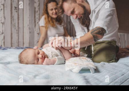 Padre che cambia il pannolino della figlia a letto a casa Foto Stock