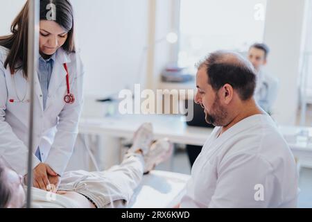 Medici che forniscono assistenza medica; paziente che riceve terapia di infusione e trattamento vitaminico in camera d'ospedale. Competenza, professionalità e compassione Foto Stock