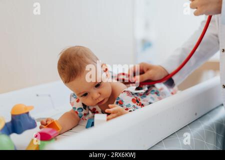 Un pediatra che esamina attentamente un bambino carino e malato per la diagnosi e il trattamento in un ambiente tranquillo e interno. Foto Stock