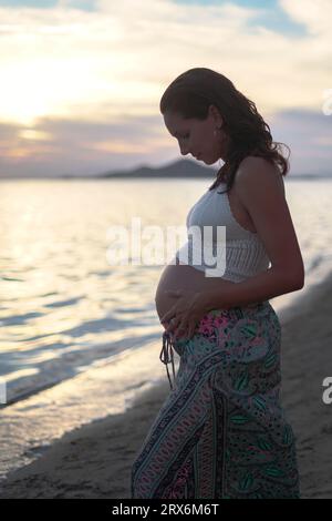 Donna incinta che tocca lo stomaco in spiaggia Foto Stock