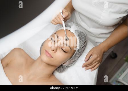 Dermatologo che applica una buccia chimica con pennello sul viso della donna Foto Stock