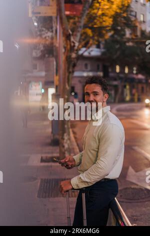 Uomo d'affari sorridente in piedi con lo smartphone sul sentiero Foto Stock