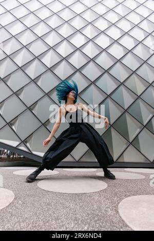 Ballerina con capelli blu tinti che balla vicino a un edificio moderno Foto Stock