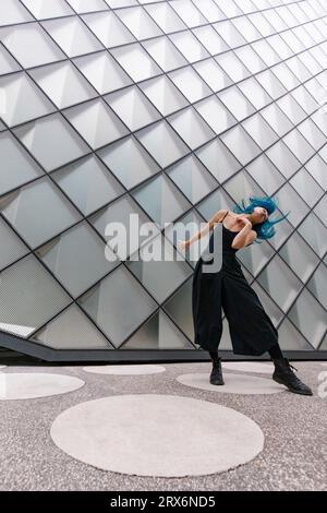 Giovane ballerina con capelli blu tinti che ballano vicino a un edificio moderno Foto Stock