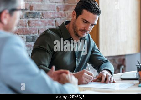 Uomo d'affari con un collega che firma un contratto in ufficio Foto Stock