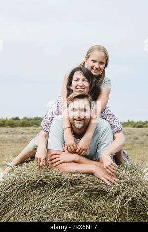 Famiglia felice insieme sul fieno in campo Foto Stock