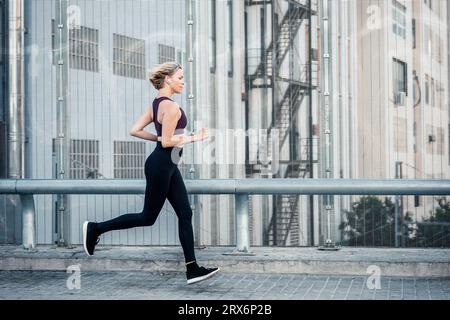 Donna che indossa cuffie intrauricolari wireless in prossimità di corrimano Foto Stock