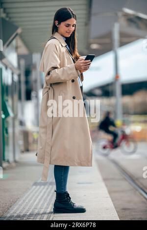 Donna sorridente che usa uno smartphone alla stazione del tram Foto Stock