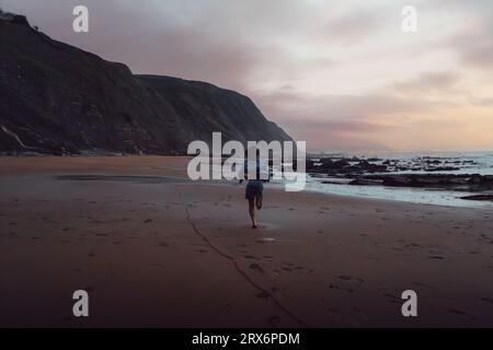 Giovane che corre sulla sabbia in spiaggia Foto Stock