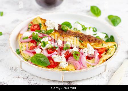 Omelette con pomodori, feta e cipolla rossa su piatto bianco. Frittata - omelette italiane. Foto Stock