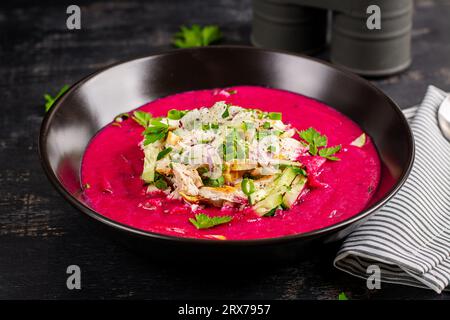Borscht freddo, zuppa estiva di barbabietole con cetriolo fresco, uovo sodo e filetto di pollo bollito su tavola scura. Cucina tradizionale europea, pranzo delizioso. Foto Stock