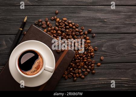 Tazza di caffè con grani di caffè e blocco note su tavole scure. Foto di alta qualità Foto Stock