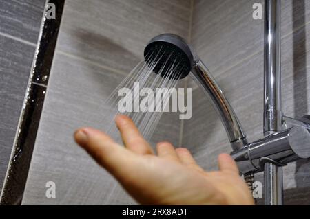 Mano dell'uomo che controlla la temperatura dell'acqua della doccia. Conforto. Foto Stock