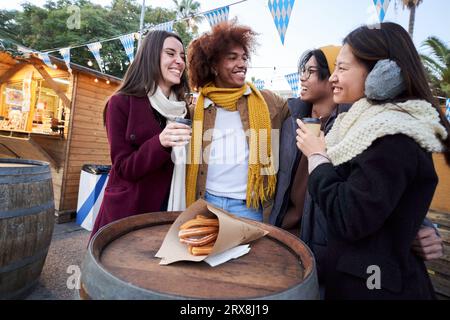 Felici amici sorridenti che mangiano cioccolato con churros insieme in strada all'aperto. Festival d'inverno. Foto Stock