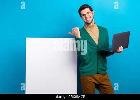 Foto di un'attraente azienda proprietaria di un giovane uomo che punta il dito con uno sconto sul laptop per gli utenti isolati su sfondo blu Foto Stock