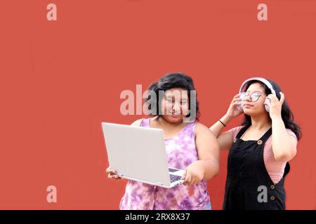 Due giovani donne latine di 20 anni usano il computer portatile e le cuffie per studiare e divertirsi guardando video musicali Foto Stock