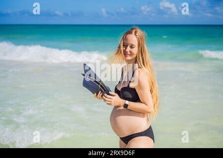 Radiosa donna incinta in costume da bagno, sullo sfondo mozzafiato di un mare turchese. Bellezza serena della maternità vicino alla riva Foto Stock