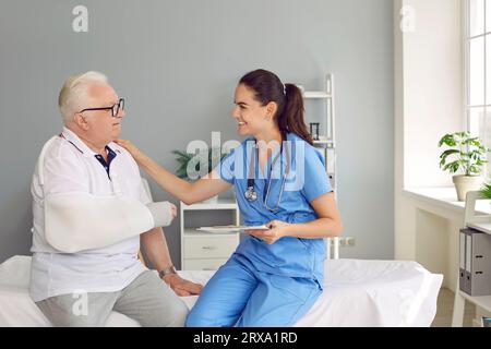 Medico sorridente e amichevole che sostiene e parla con un paziente anziano con un braccio rotto Foto Stock