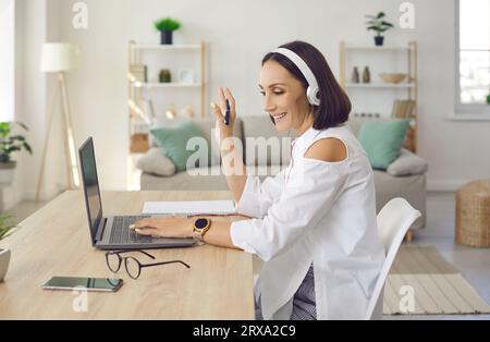 Donna in cuffia che saluta lo schermo del notebook all'inizio di una videochiamata Foto Stock