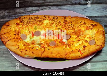 Formaggio Fougasse condito con fette di peperoni verdi, formaggio e salsiccia tagliata cotta in forno, il pane alla fougasse è un tipo di pane tipicamente associato Foto Stock