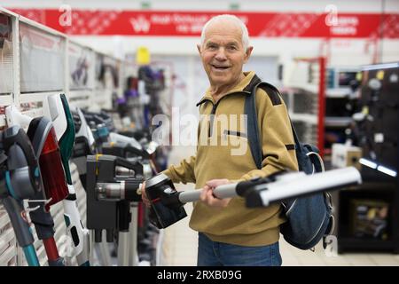 Uomo anziano che sceglie un aspirapolvere verticale nello showroom del negozio di elettrodomestici Foto Stock