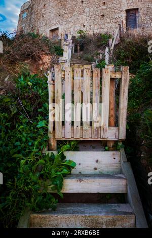 Scalini e cancelli in legno usurati che conducono in salita a un'antica fortezza in pietra Foto Stock