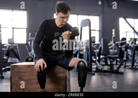 Un giovane, forte, bello e motivato, con disabilità e una gamba protesica, si allena in una palestra con manubri. Poster della motivazione. copiare lo spazio, la vita Foto Stock