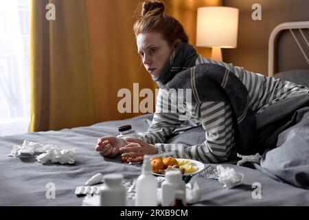 donna rossa seria con naso che cola che soffia freddo e gola gonfia seduta sul letto a casa. donna in camera da letto, con pillole di medicamenti. donna malata io Foto Stock