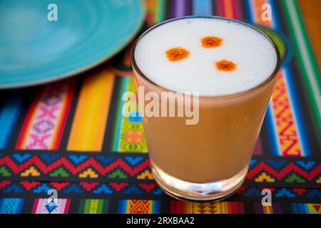 Bevanda alcolica Pisco Sour, cocktail peruviano, a base di Pisco (grappe di uva peruviana), succo di lime, sciroppo e albume d'uovo, in bicchiere su tovaglioli con motivi tradizionali. Messa a fuoco selettiva, sfondo sfocato, messa a fuoco sul vetro anteriore e sulla schiuma. Foto Stock