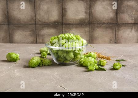 Recipiente in vetro con luppolo verde fresco e grano su tavolo grigio Foto Stock