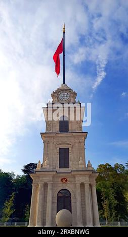 Una torre dell'orologio con sopra una bandiera, cielo blu Foto Stock