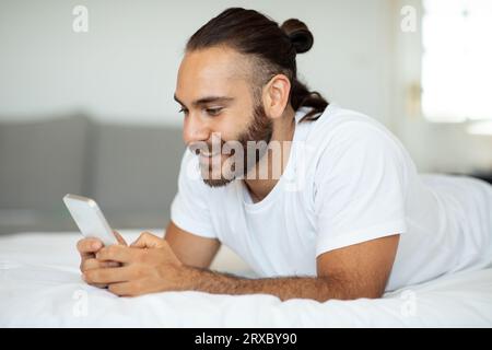Un giovane felice che usa il telefono a letto dopo essersi svegliato Foto Stock